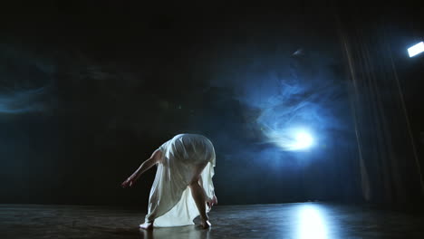 Elegant-ballerina-jumping-and-dancing-in-barefoot-and-white-loose-oversize-dress-in-studio.-With-smoke